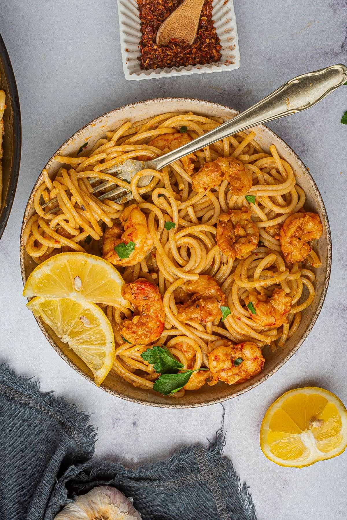 Cajun shrimp scampi, a spicy Cajun pasta recipe, is in a bowl with a fork and lemon wedges.