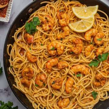 Cajun shrimp scampi made with spaghetti in a large skillet with lemon wedges.