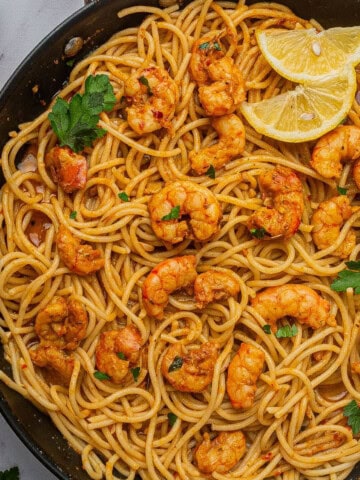 Cajun shrimp scampi made with spaghetti in a large skillet with lemon wedges.