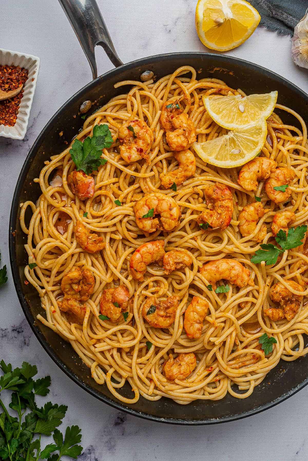 Cajun shrimp scampi made with spaghetti in a large skillet with lemon wedges.