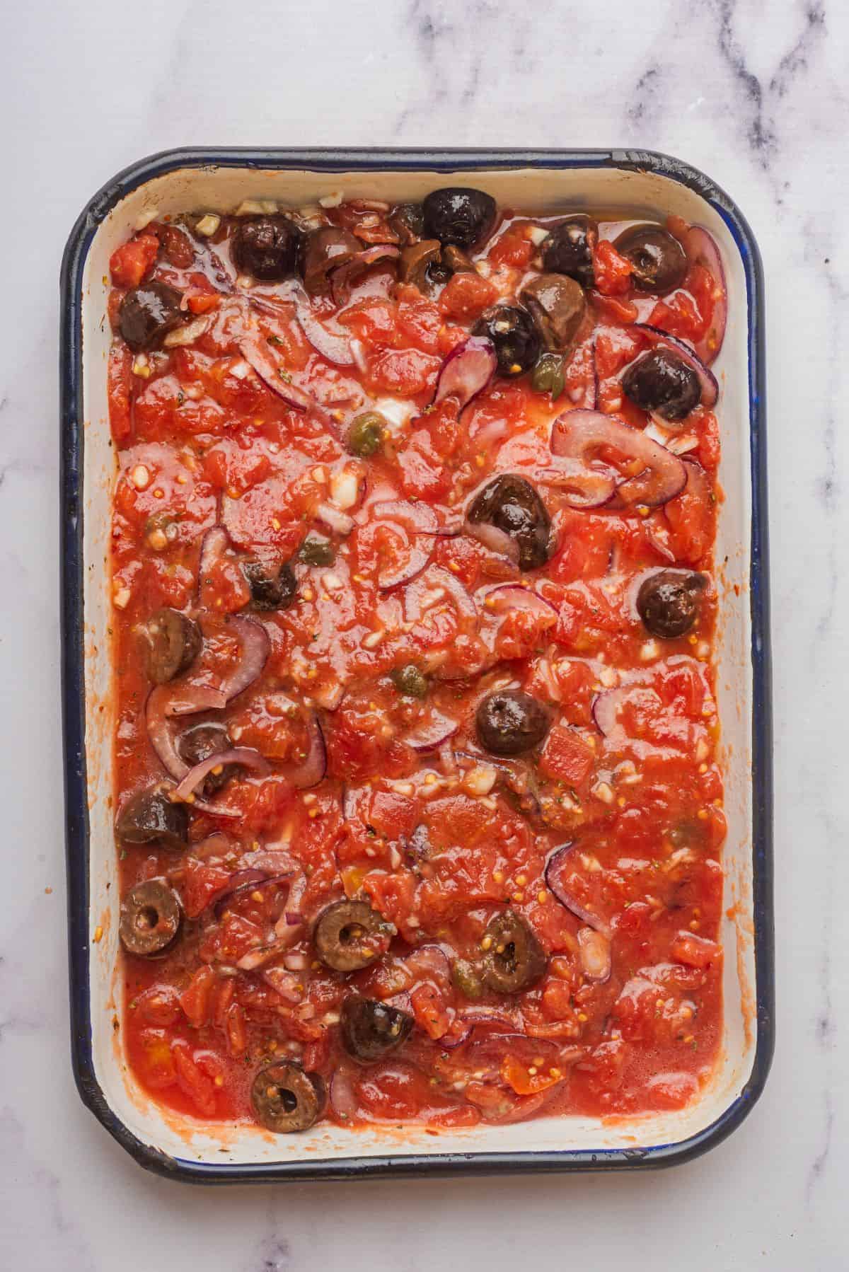 Ingredients for puttanesca sauce are combined in a baking dish.