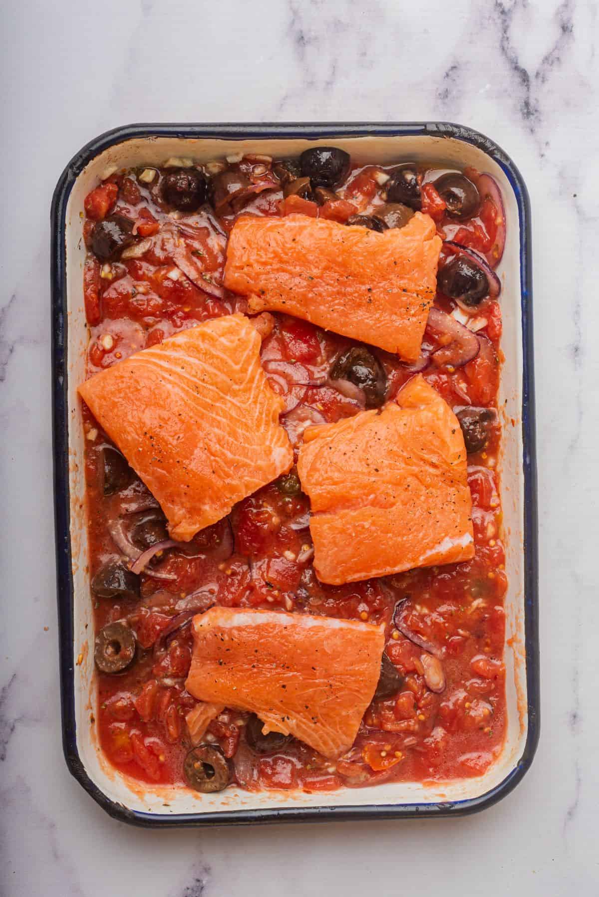 Salmon with tomato sauce is in a baking dish.