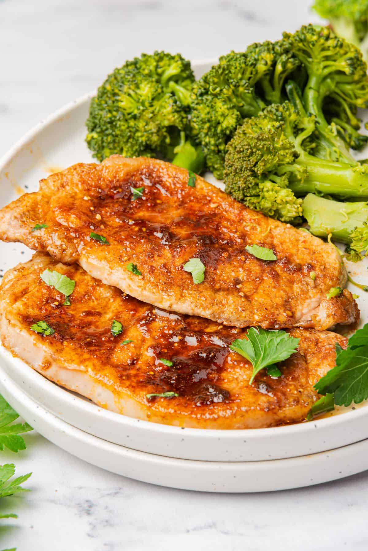 Two air fryer thin pork chops on a plate with a side of broccoli.