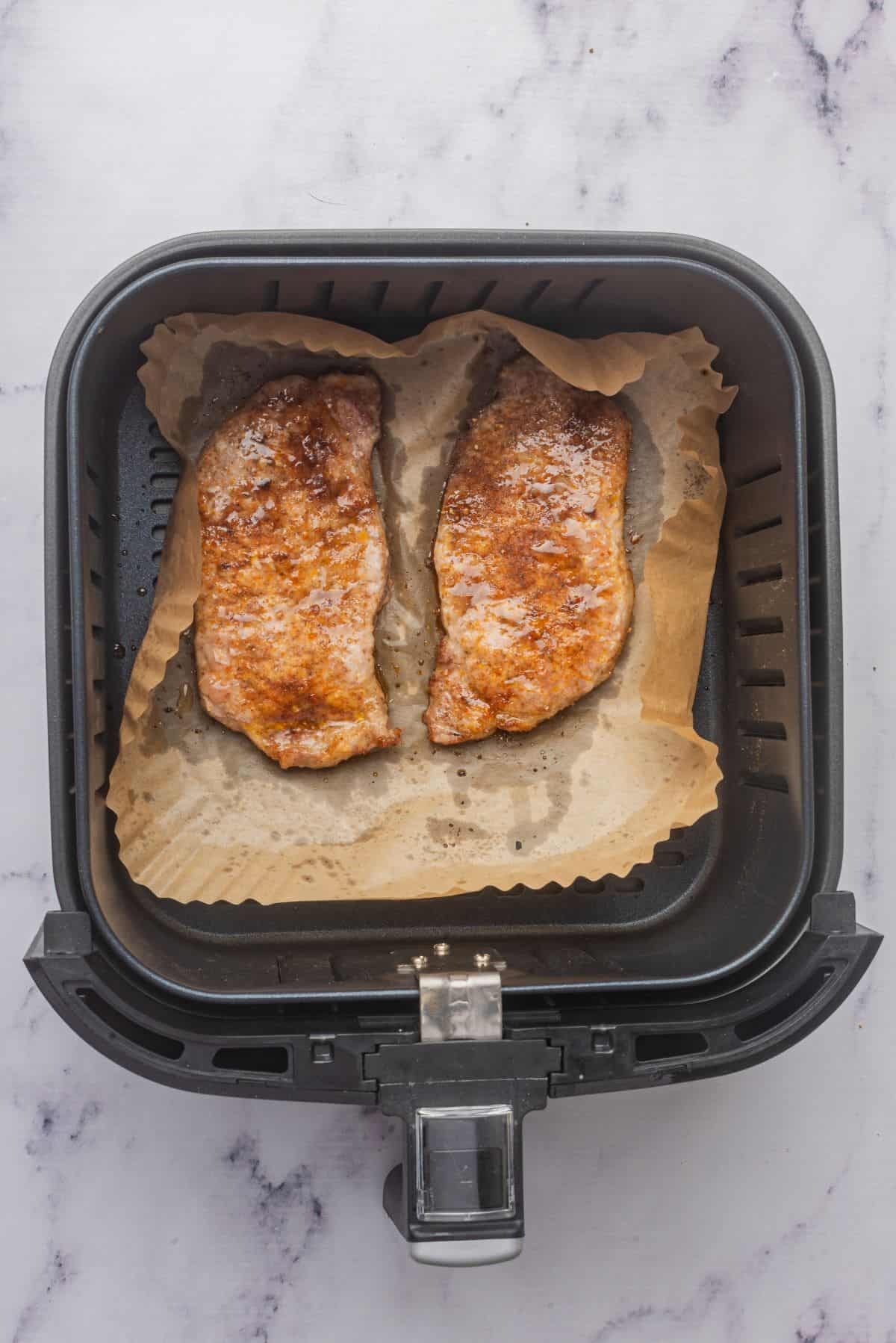 Two cooked thin boneless pork chops in air fryer basket.