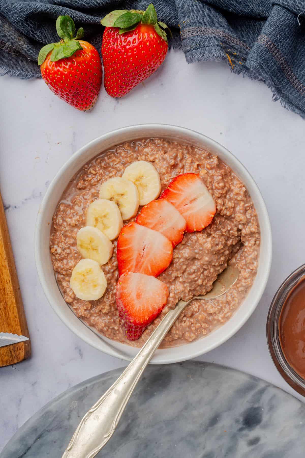 Nutella oatmeal in a bowl with a spoon and topped with sliced banana and strawberry.