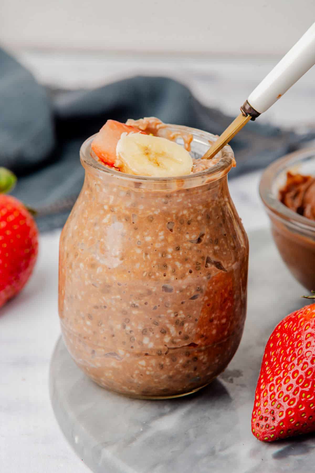 Nutella overnight oats in a jar with sliced banana and strawberry.