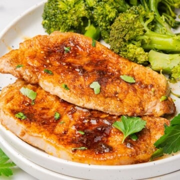 Two air fryer thin pork chops on a plate with a side of broccoli.