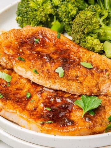 Two air fryer thin pork chops on a plate with a side of broccoli.