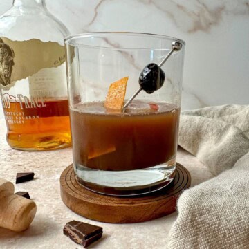 Chocolate old fashioned in a rocks glass with an orange peel and cherry garnish.