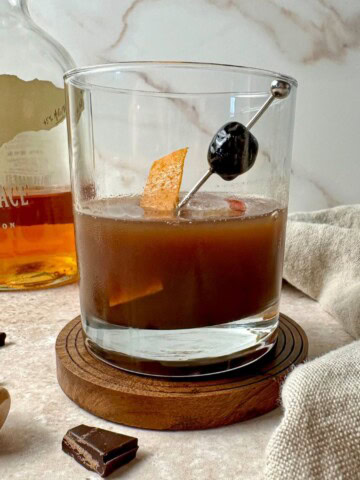 Chocolate old fashioned in a rocks glass with an orange peel and cherry garnish.