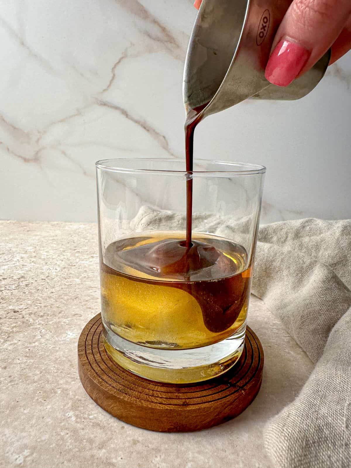 A hand pouring chocolate liqueur into a glass with bourbon.