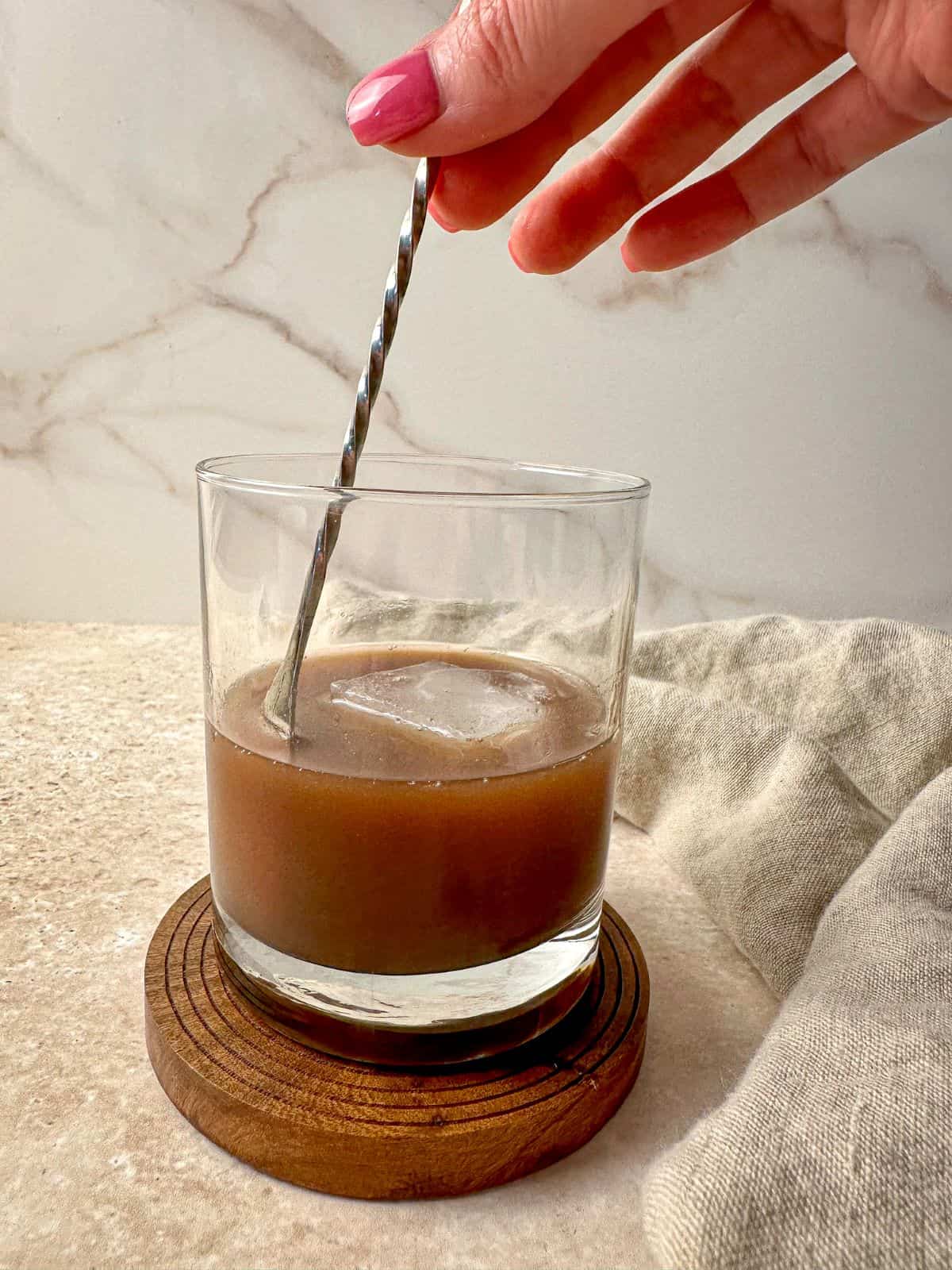 A bar spoon stirring a chocolate old  fashioned cocktail.