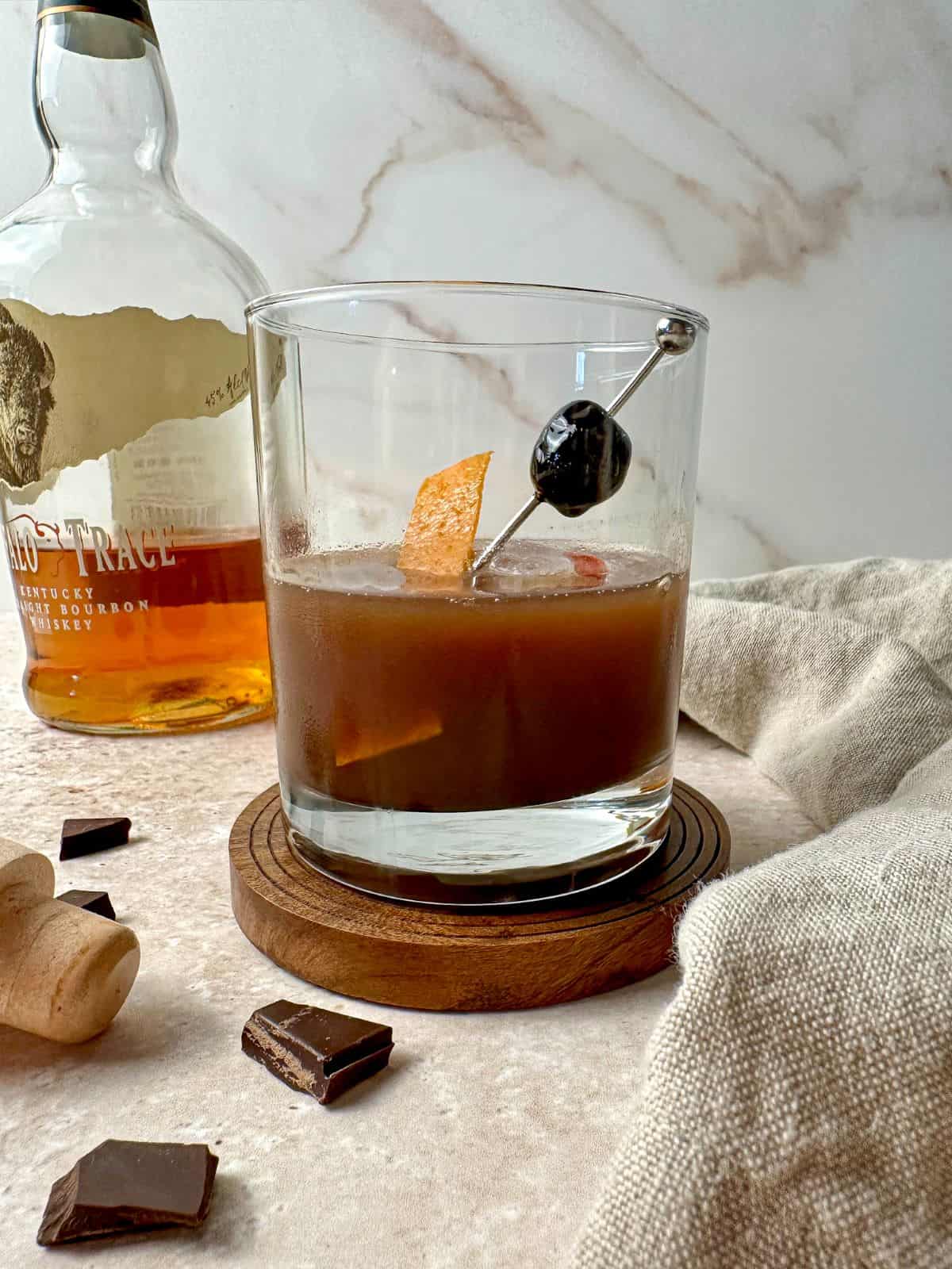 Chocolate old fashioned in a rocks glass with an orange peel and cherry garnish.