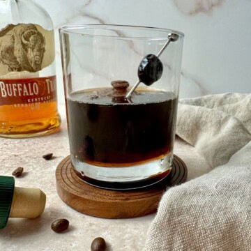 Coffee old fashioned in a rocks glass with a cherry and coffee beans for garnish.