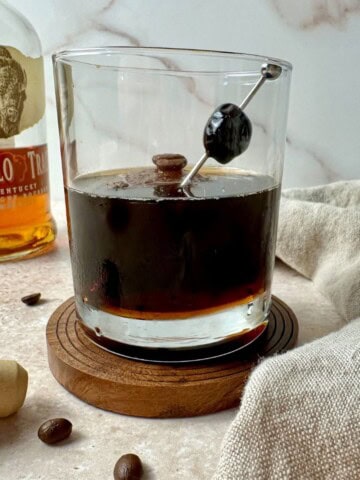 Coffee old fashioned in a rocks glass with a cherry and coffee beans for garnish.