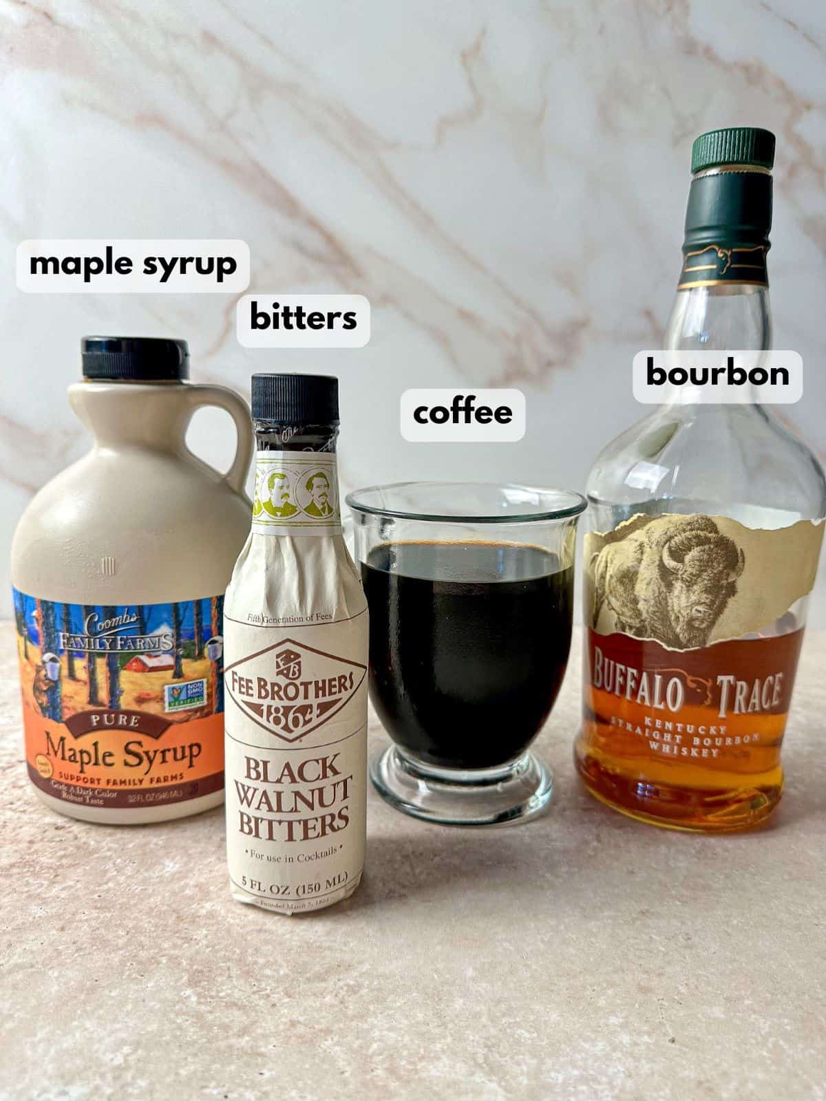 A bottle of bourbon, bitters, maple syrup, and coffee or espresso in a cup.