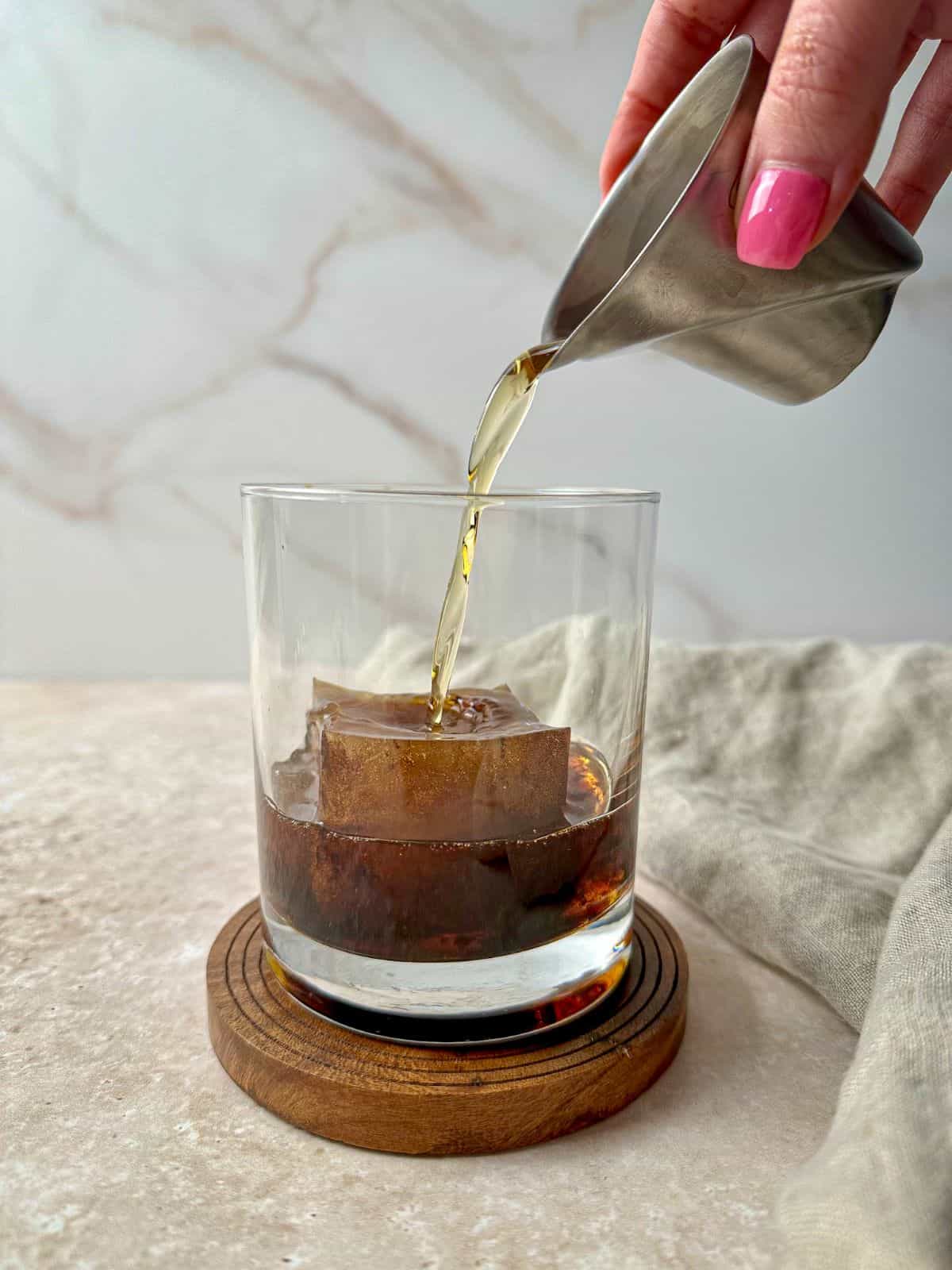 A hand pouring bourbon over a coffee ice cube.