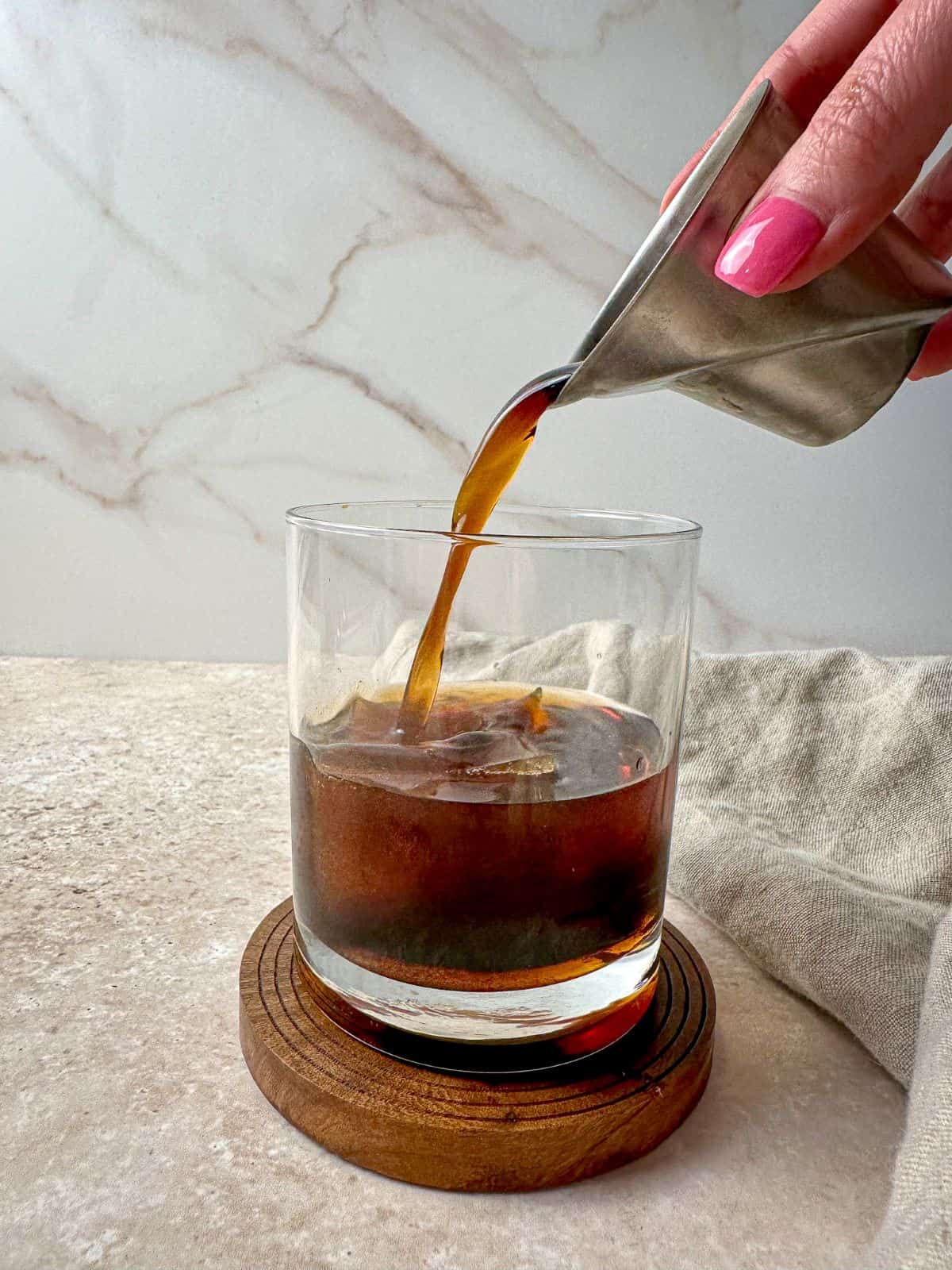 A hand pouring coffee or espresso into a rocks glass with bourbon.