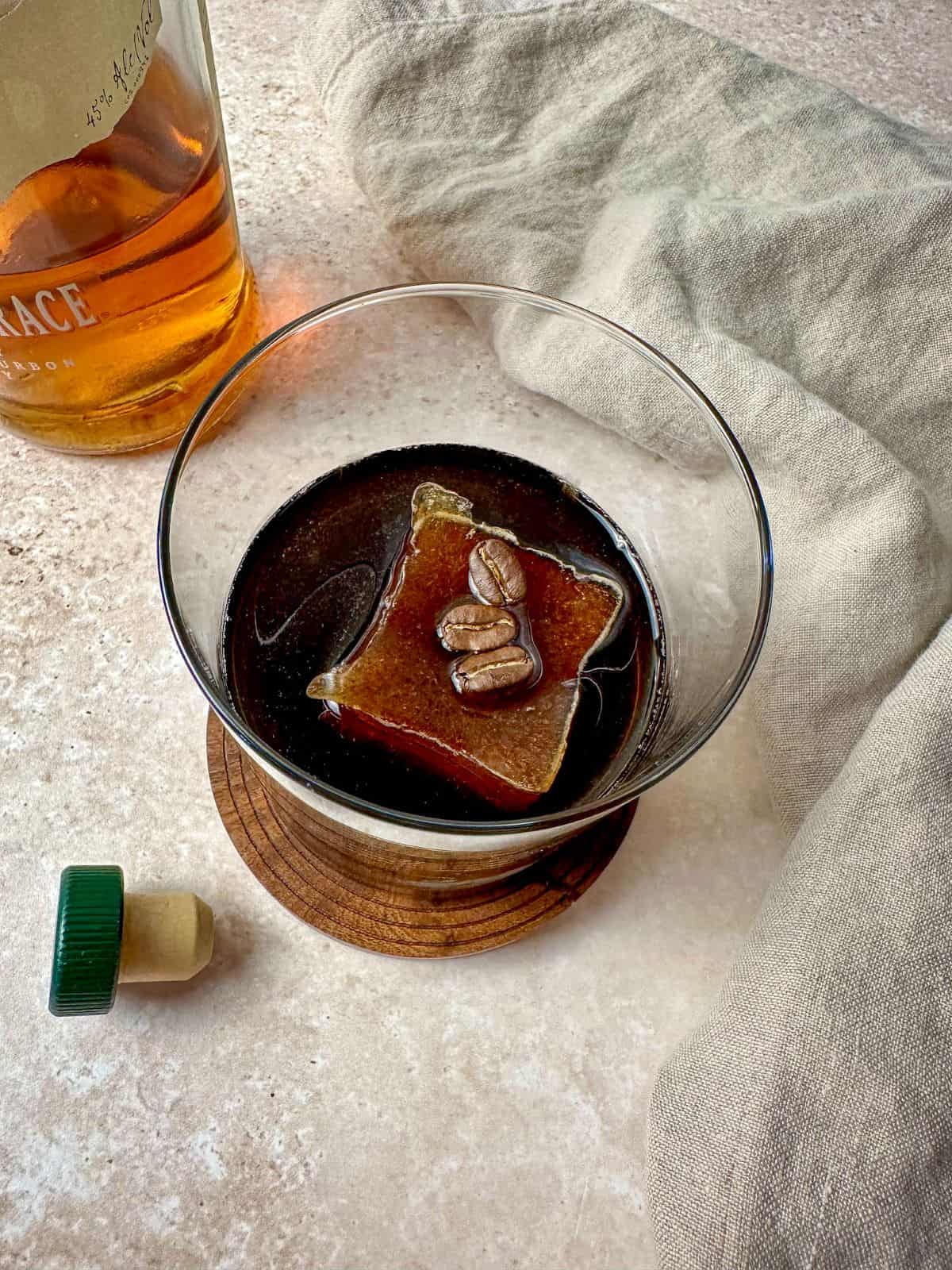 Coffee old fashioned in a rocks glass with an ice cube made with coffee and three coffee beans.