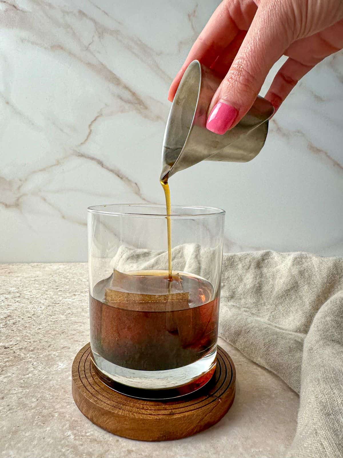 A hand pouring maple syrup into a cocktail with bourbon and coffee.