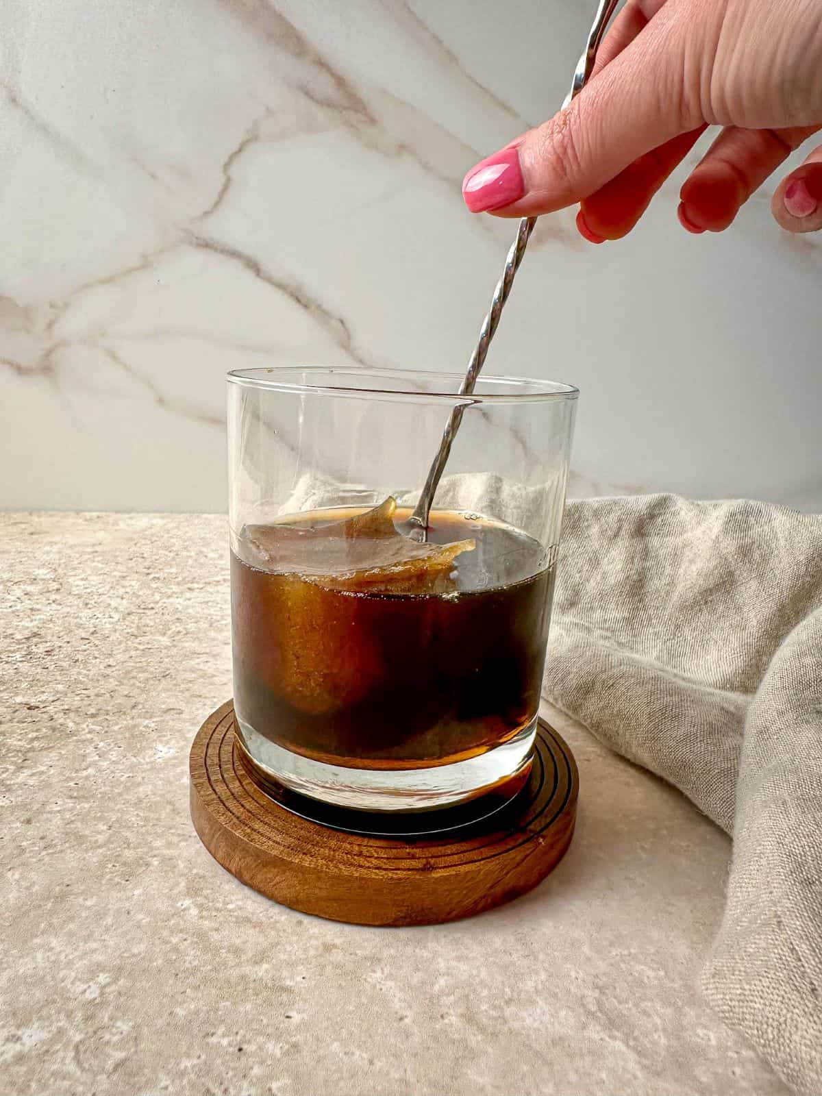 A hand using a bar spoon to stir a bourbon coffee cocktail.