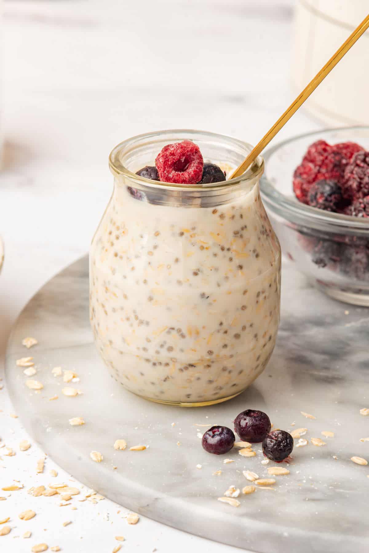 Vanilla overnight oats in a glass jar with a spoon and fresh fruit on top.