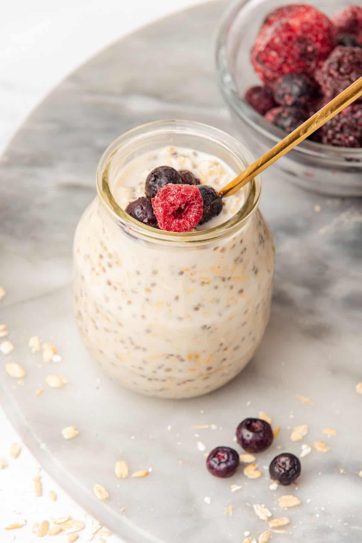 Berries on top of creamy vanilla overnight oats in a glass jar with a gold spoon.