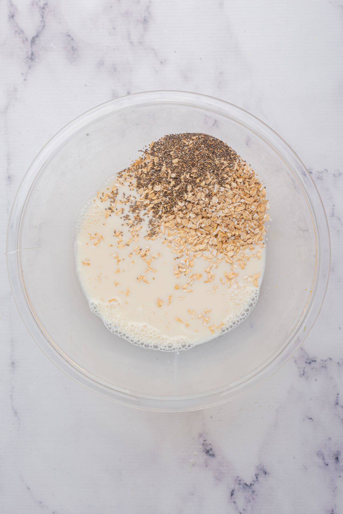 Oats and chia seeds added to a glass bowl with vanilla almond milk, maple syrup, vanilla Greek yogurt, and vanilla extract.