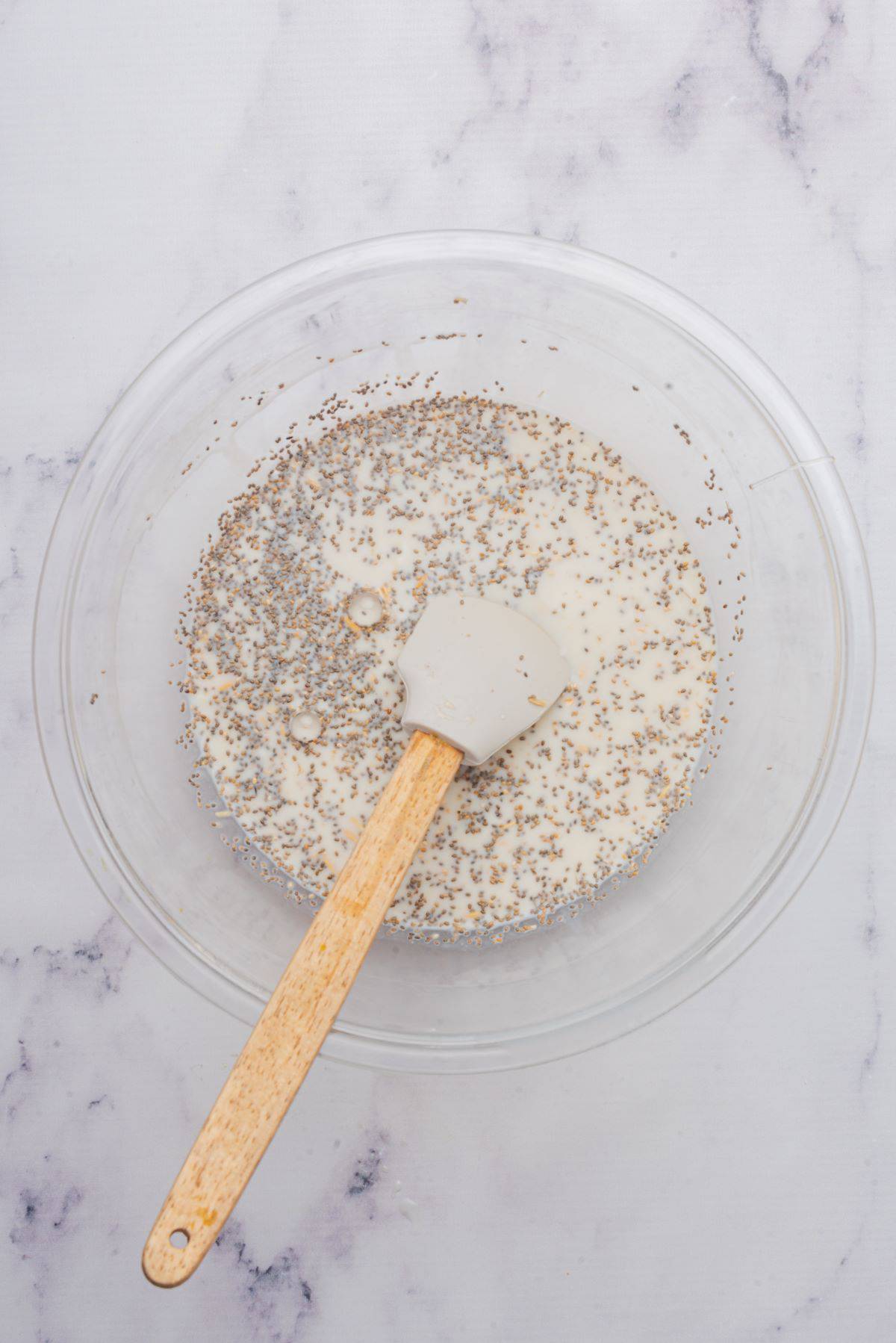 A spoon in a glass bowl stirring together all the ingredients for creamy overnight oats.