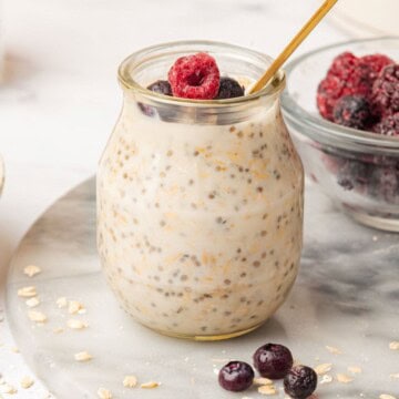 Vanilla overnight oats in a glass jar with a spoon and fresh fruit on top.