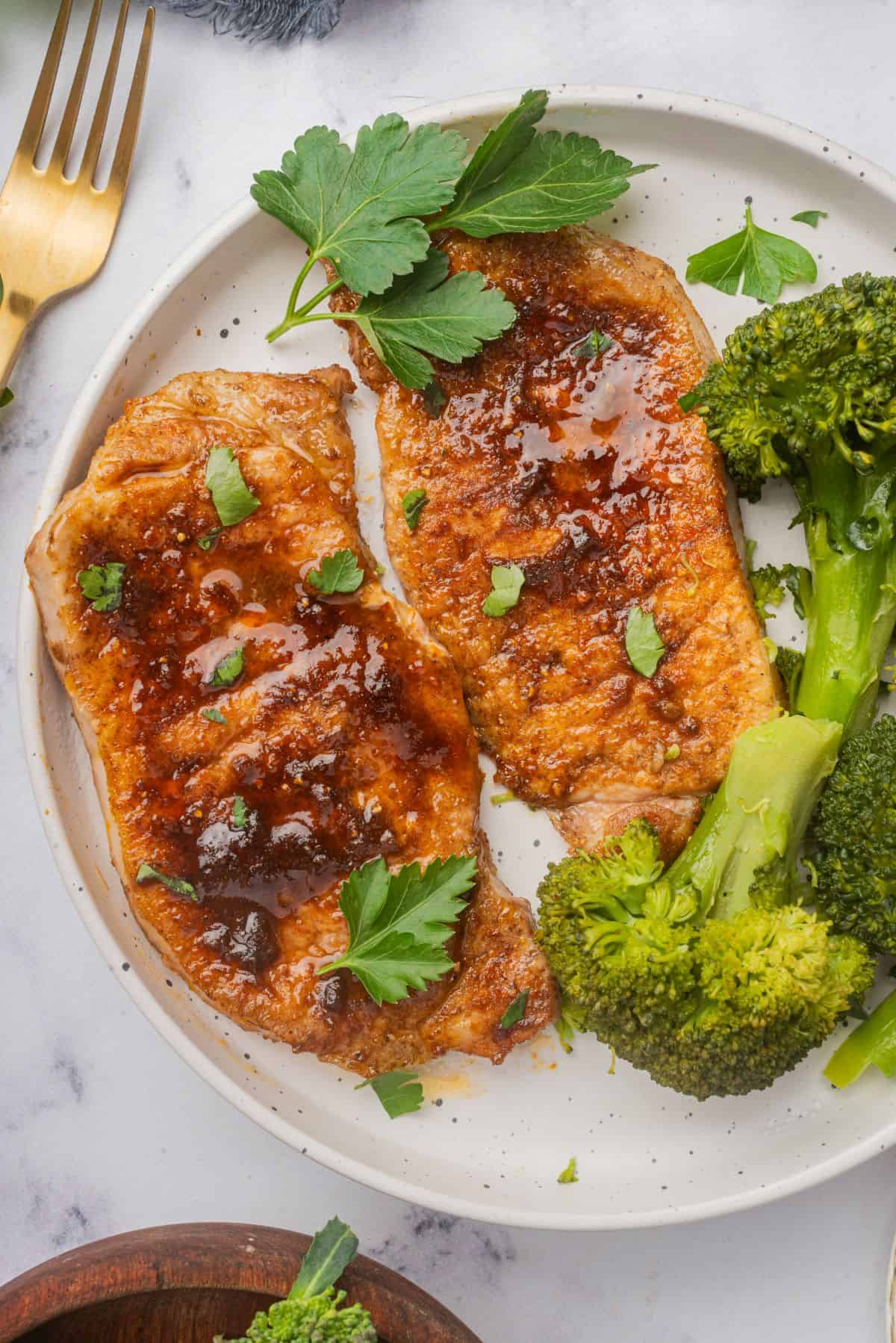 Air fryer pork chops with no breading on a plate with a side of broccoli.