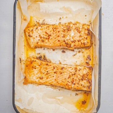 Baked blackened salmon in a baking dish with parchment paper.