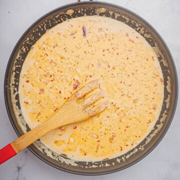 Cajun Alfredo sauce recipe cooking in a large skillet with a wooden spoon.