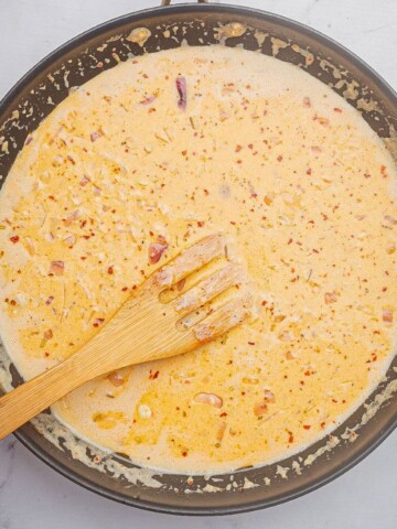 Cajun Alfredo sauce recipe cooking in a large skillet with a wooden spoon.