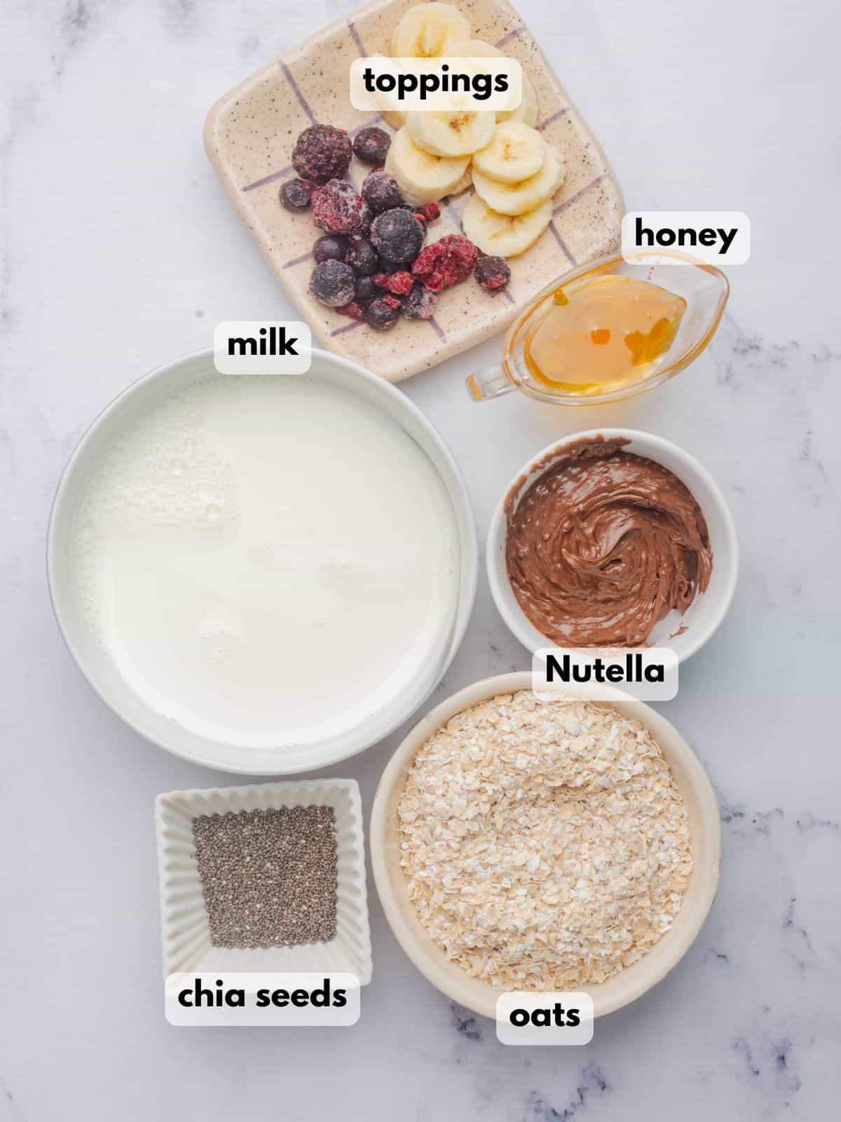 Ingredients to make overnight oats with Nutella include bowls of Nutella, oats, milk, honey, chia seeds, and bananas.