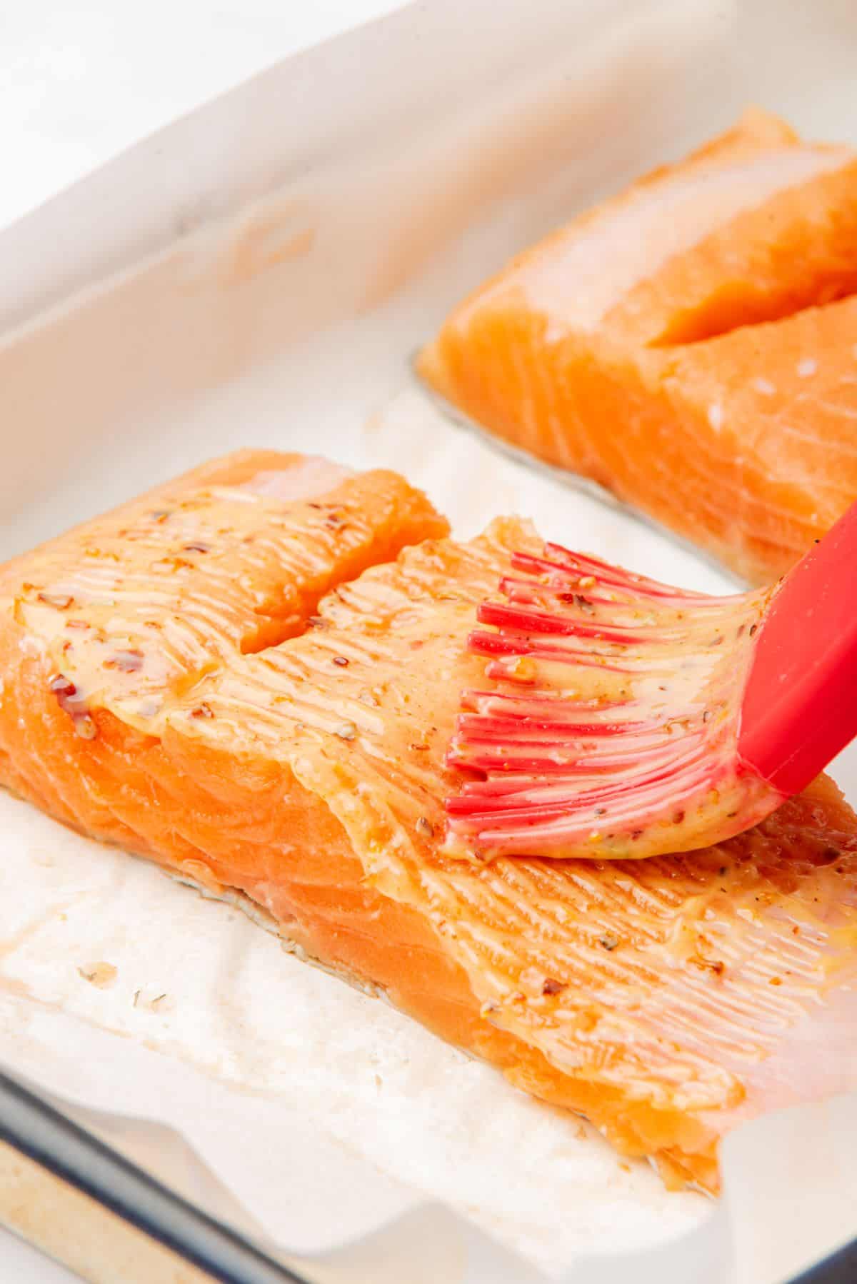 A pastry brush brushing melted butter and blackened seasoning on salmon.