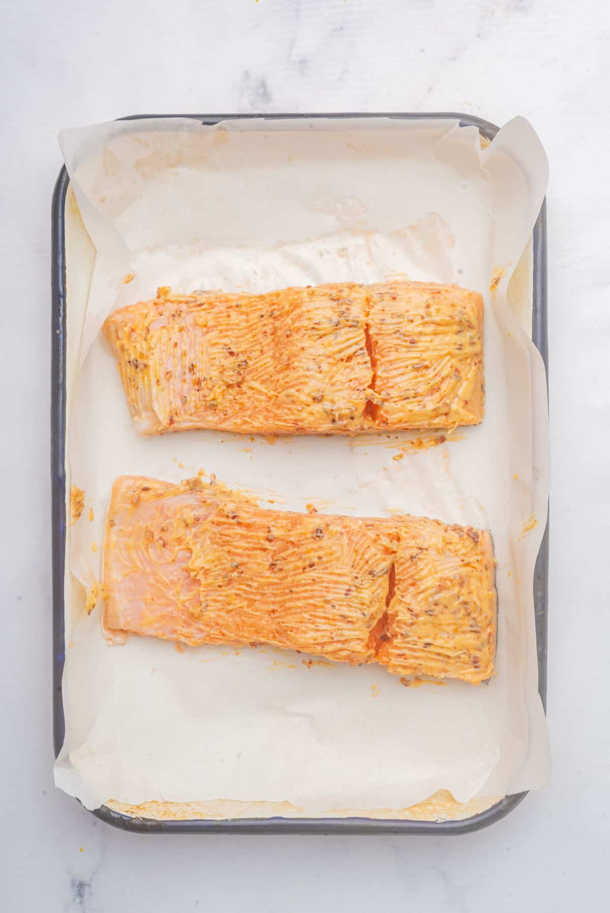 Two salmon fillets coated in butter and blackened seasoning in a baking dish. 