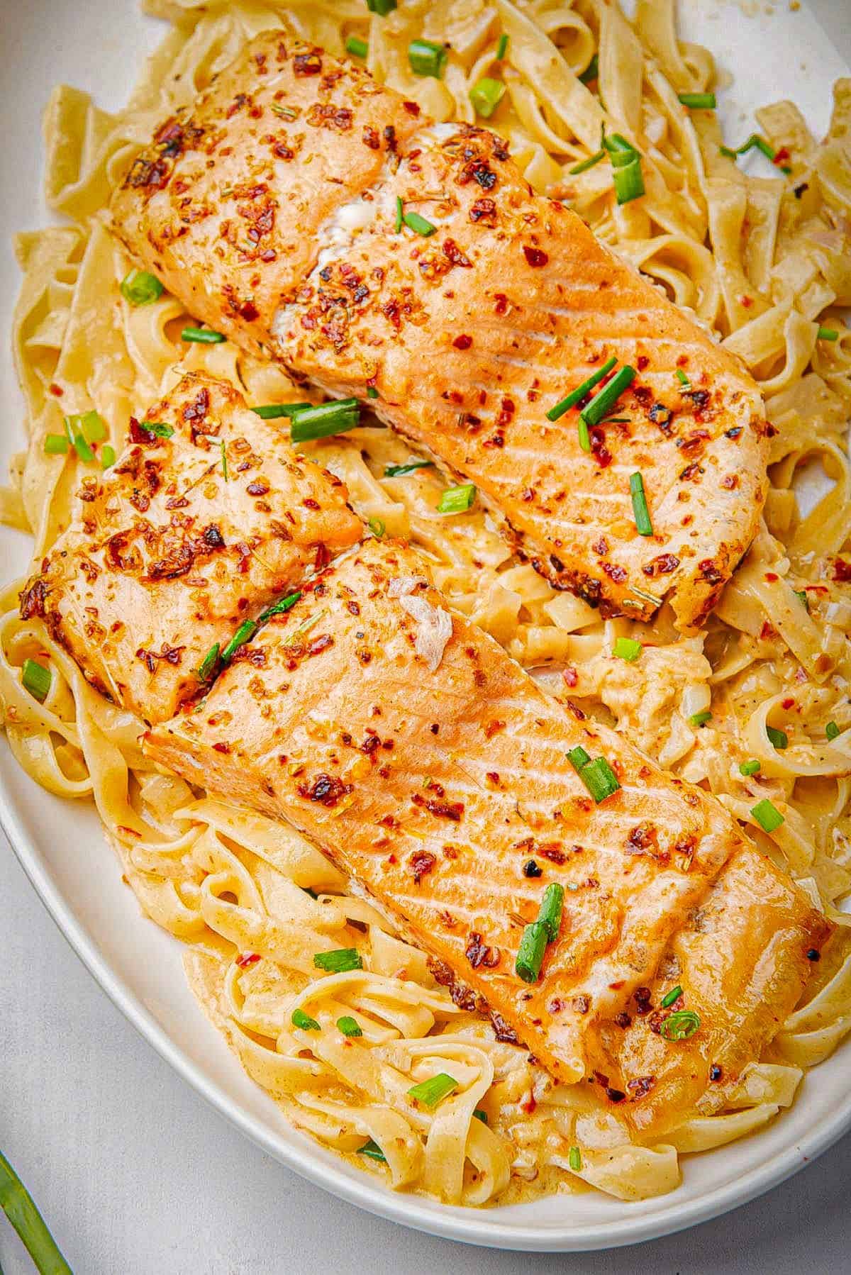 Two baked blackened salmon fillets on a bed of pasta.