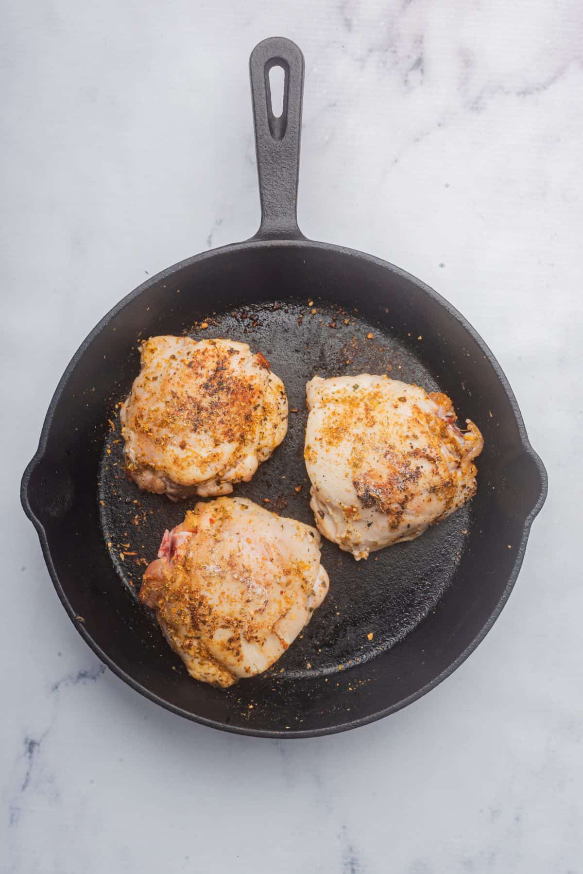 Italian seasoned chicken thighs searing in a cast iron skillet.