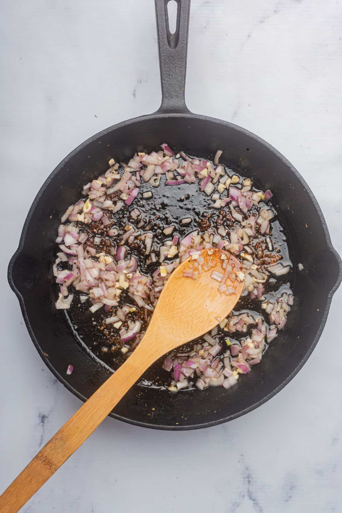 Minced garlic and shallots sautéing in a skillet with a wooden spoon.