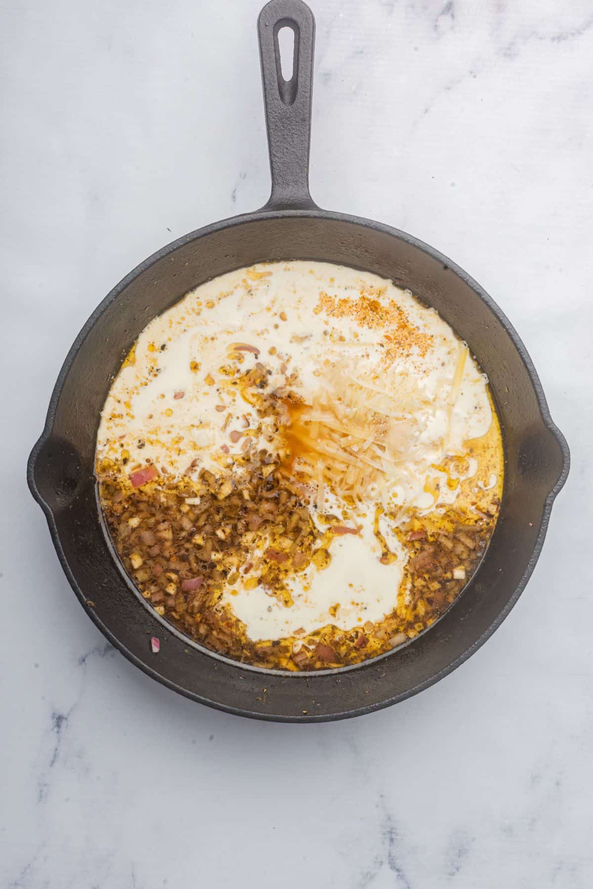 Heavy cream, parmesan cheese, and Italian seasoning simmering in a skillet. 