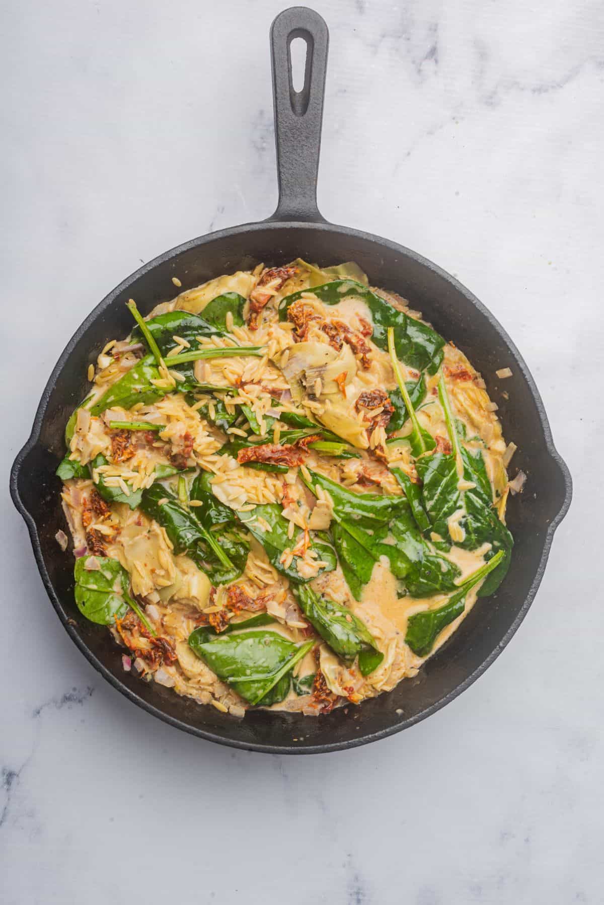 Orzo pasta, spinach, artichokes, and tomatoes added to the ovenproof skillet.