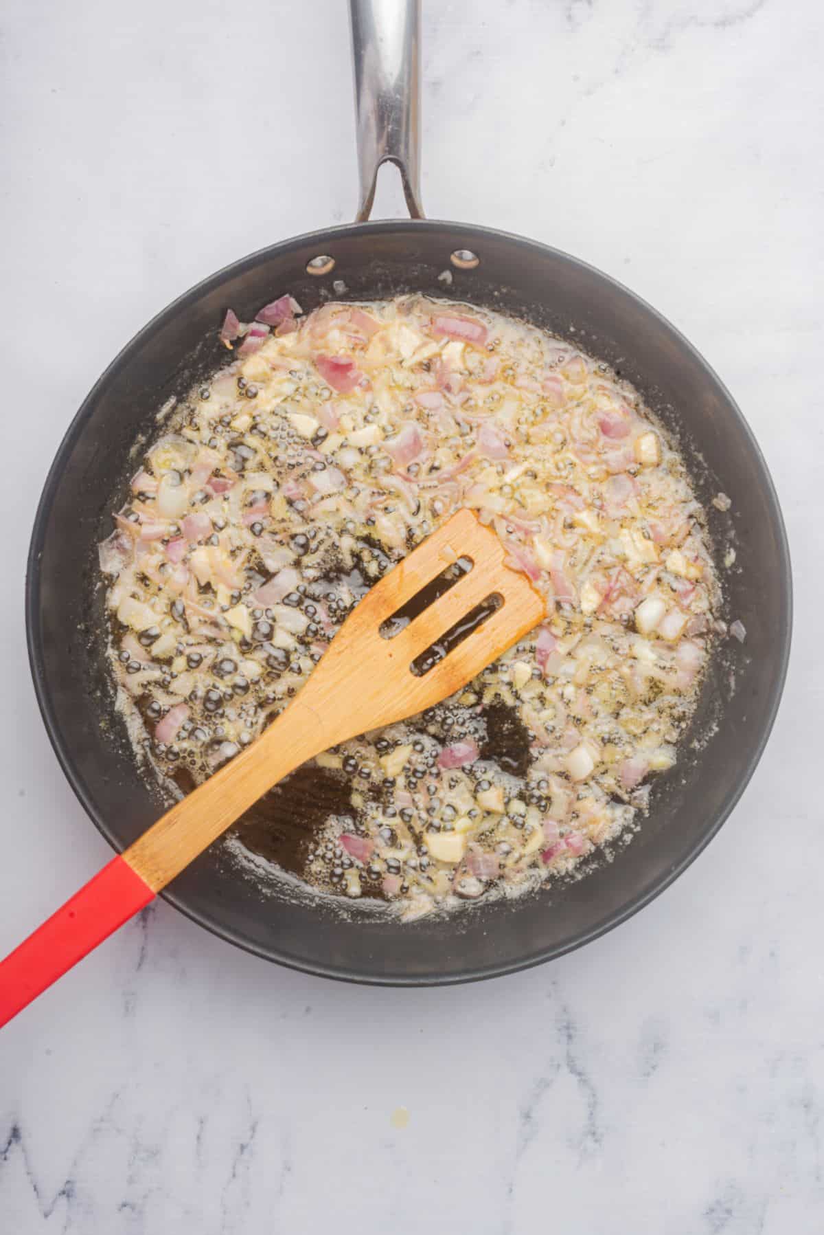 Butter, garlic, and shallots sauteing in a skillet.