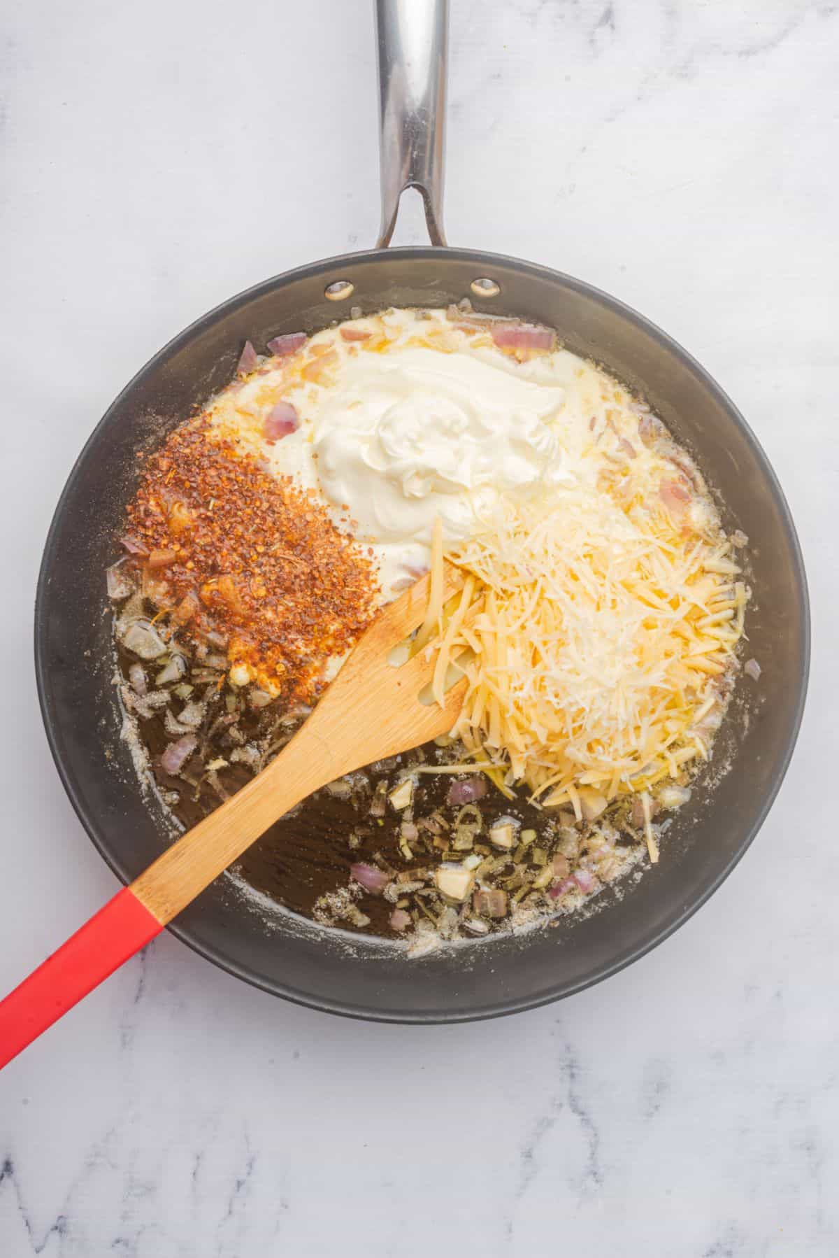 Making homemade Cajun Alfredo sauce in a skillet with a wooden spoon.