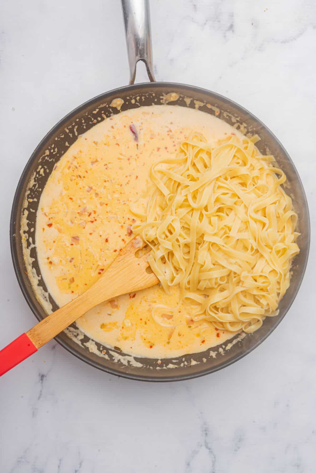 Cajun salmon Alfredo sauce in a skillet with pasta and a wooden spoon.