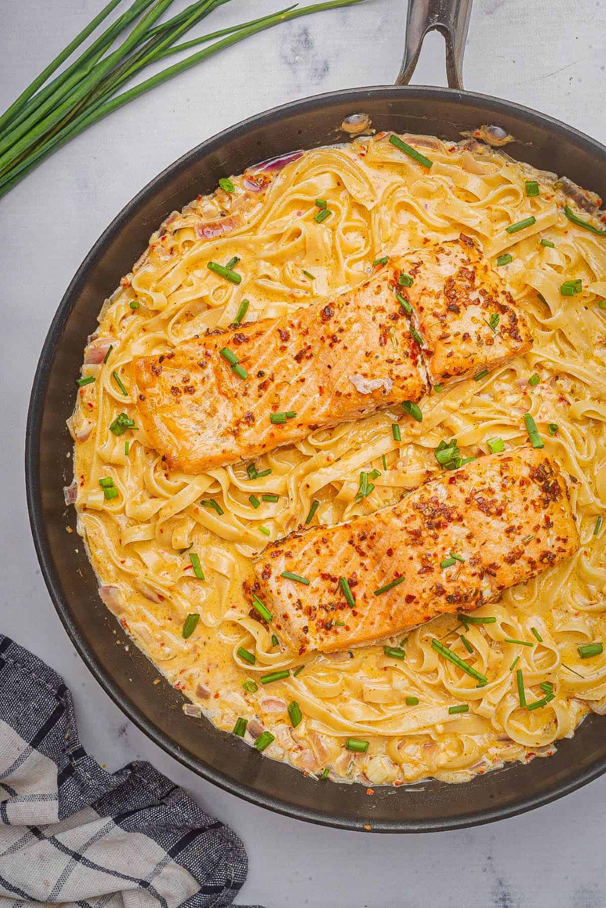 Cajun salmon pasta in a skillet topped with chives.