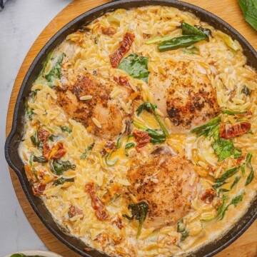 Baked chicken and orzo pasta in a skillet with spinach, artichoke hearts, and sun-dried tomatoes.