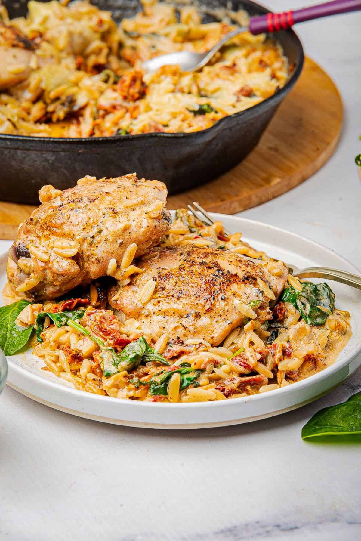 Chicken orzo bake on a plate with two chicken thighs and creamy orzo pasta.