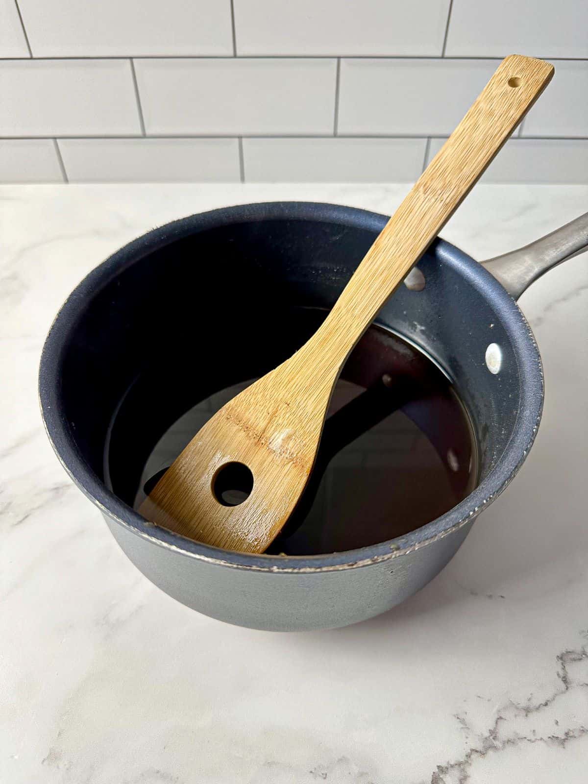 A small saucepan containing simple syrup with brown sugar and a wooden spoon.