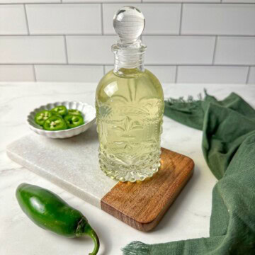 Jalapeno simple syrup in a glass jar with a bowl of sliced jalapenos.